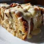 A close-up of a moist slice of bread pudding topped generously with vanilla cream sauce.