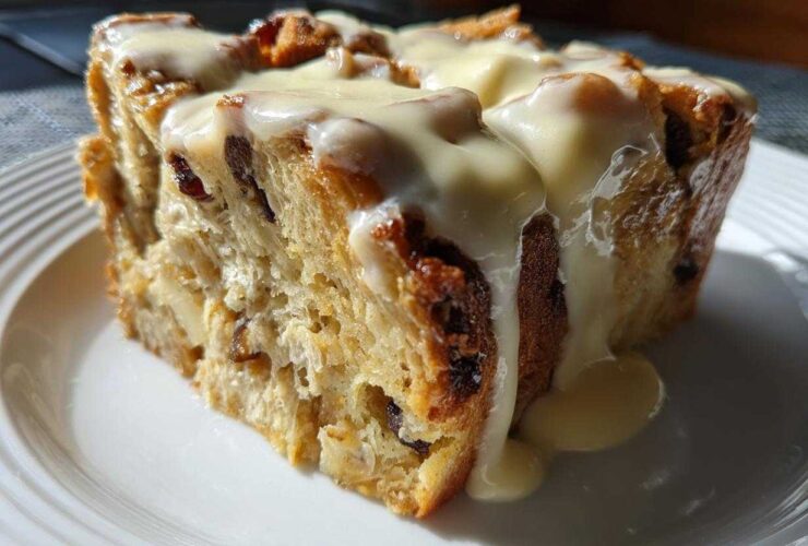 A close-up of a moist slice of bread pudding topped generously with vanilla cream sauce.