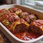 A white baking dish filled with homemade cabbage rolls smothered in rich tomato sauce.