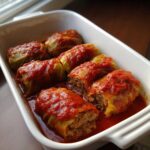 Six homemade cabbage rolls stuffed with meat filling, baked in a white dish with rich tomato sauce.