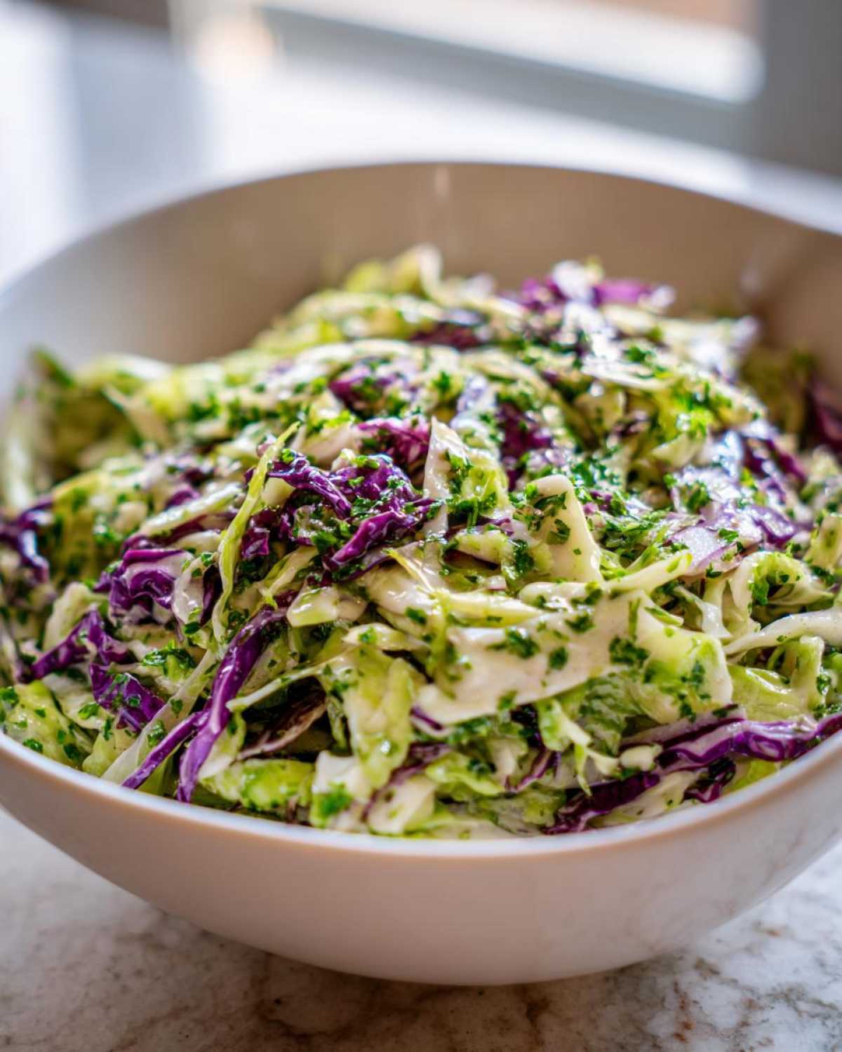 A close-up of a vibrant cabbage salad featuring shredded green and purple cabbage tossed in a light dressing and fresh herbs.