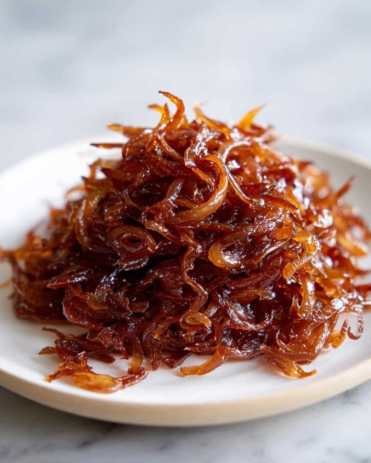 A close-up of a rich, dark brown caramelized onions served on a white plate.