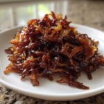 A mound of deeply browned, glossy caramelized onions piled high on a small white serving dish.