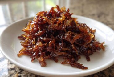 A mound of deeply browned, glossy caramelized onions piled high on a small white serving dish.