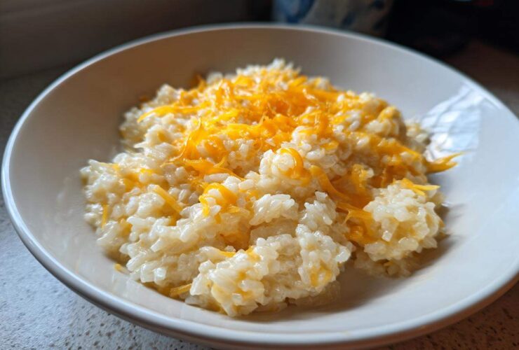 A close-up of a white bowl filled with creamy, amazing cheesy rice topped generously with melted shredded cheddar cheese.