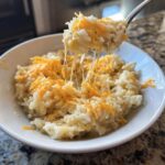 A fork lifting a spoonful of amazing cheesy rice, showing long, melted cheese strings pulling away from the bowl.