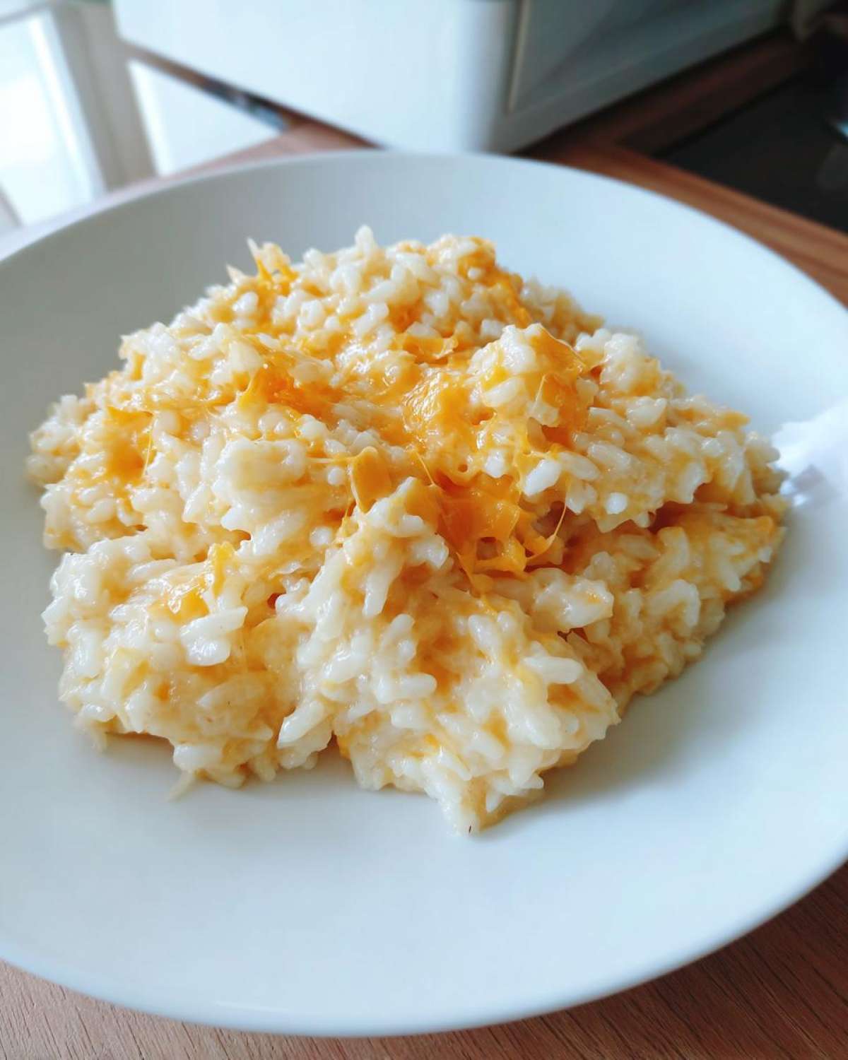 A close-up serving of creamy, white rice topped with melted orange cheddar cheese, representing amazing cheesy rice.
