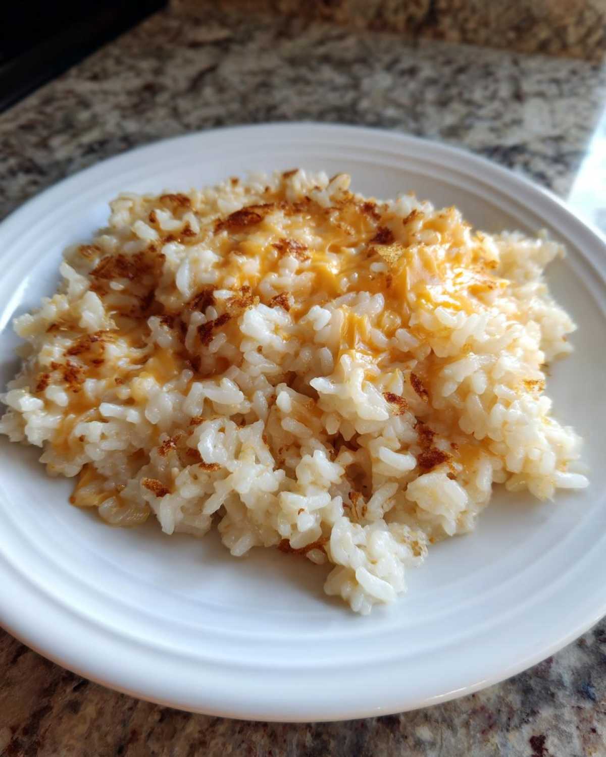 A close-up of a serving of fluffy white rice topped with melted orange cheddar cheese, creating amazing cheesy rice.