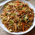 A close-up of a large white bowl filled with homemade chicken chow mein recipe, featuring noodles, chicken pieces, and stir-fried vegetables.