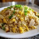 A close-up of a mound of amazing chicken fried rice, featuring rice, scrambled egg, chicken pieces, and green onions.