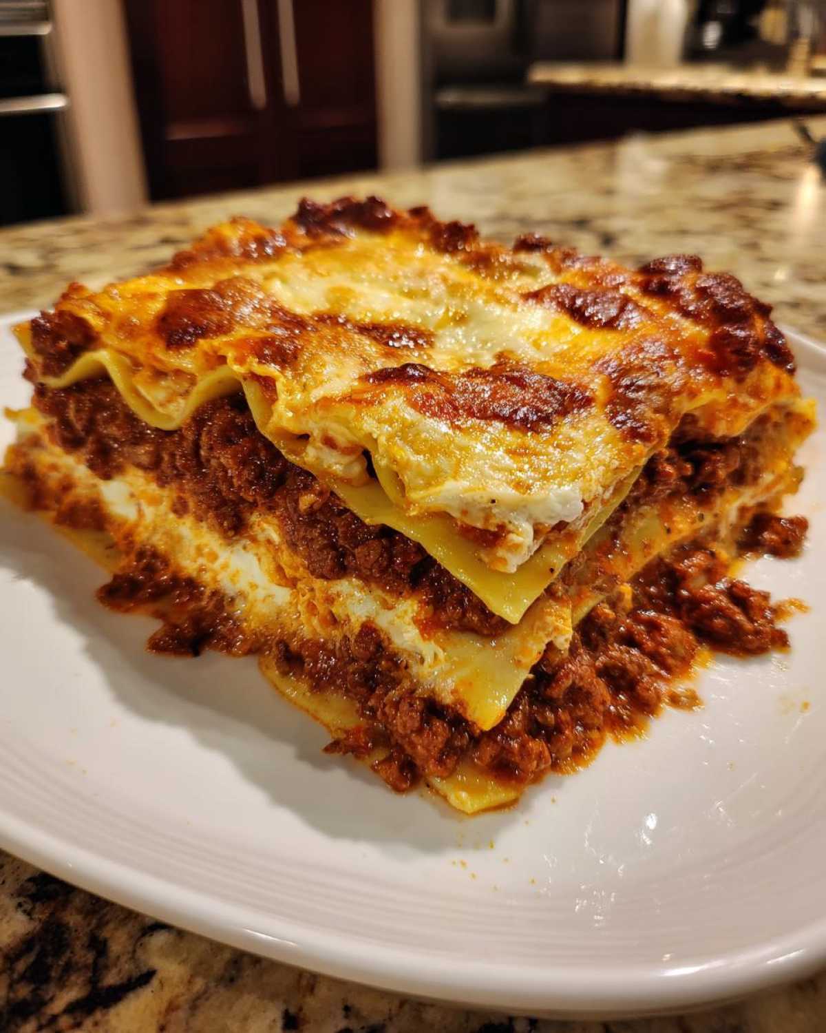 A thick, layered slice of baked lasagna with rich meat sauce and melted cheese topping on a white plate.