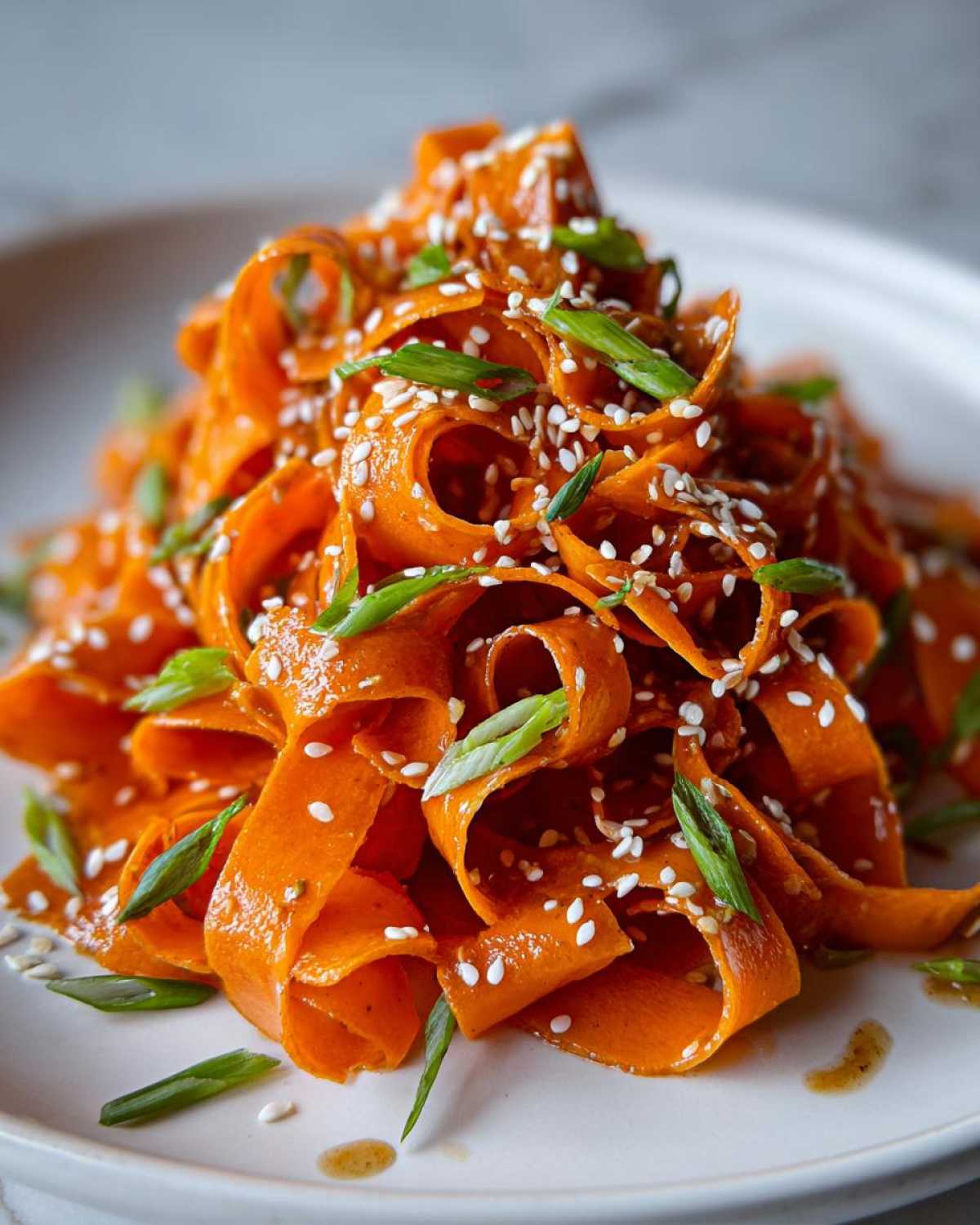 Close-up of a vibrant raw carrot salad made with shaved carrot ribbons, topped with sesame seeds and green onions.