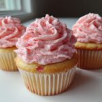 Three delicious strawberry cupcakes topped with swirled pink frosting speckled with strawberry pieces.