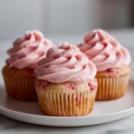 Three delicious strawberry cupcakes topped with swirls of pink strawberry frosting sitting on a white plate.