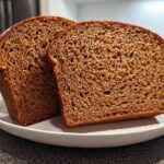 Two thick slices of dark, moist whole wheat bread displayed on a white plate.