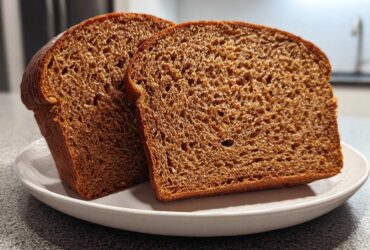 Two thick slices of dark, moist whole wheat bread displayed on a white plate.