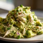 A close-up, appetizing serving of creamy avocado chicken salad mixed with chunks of avocado and fresh herbs.