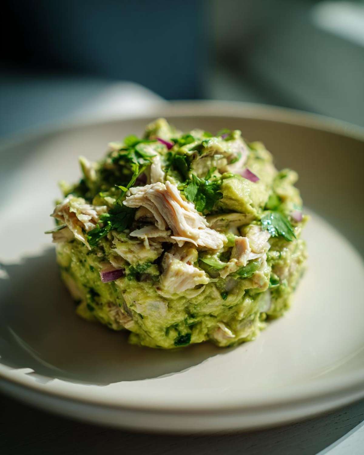 A beautiful mound of creamy avocado chicken salad topped with shredded chicken and fresh cilantro.