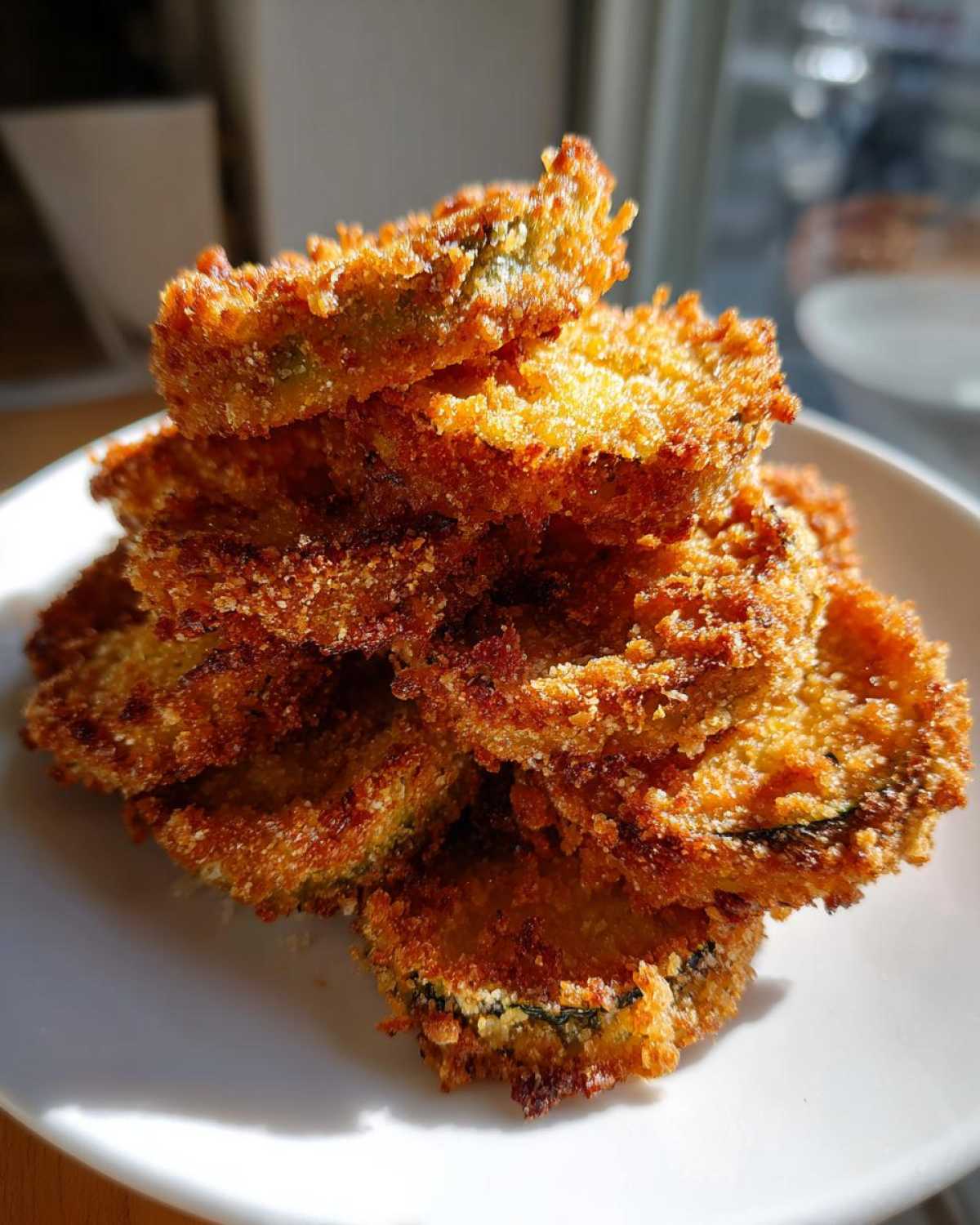 A stack of golden brown, crispy baked parmesan zucchini slices piled high on a white plate.