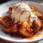 Close-up of Bananas Foster featuring caramelized bananas and a scoop of vanilla ice cream drizzled with sauce.