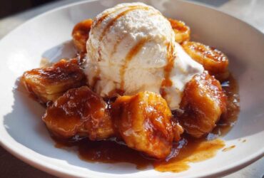 Close-up of Bananas Foster featuring caramelized bananas and a scoop of vanilla ice cream drizzled with sauce.