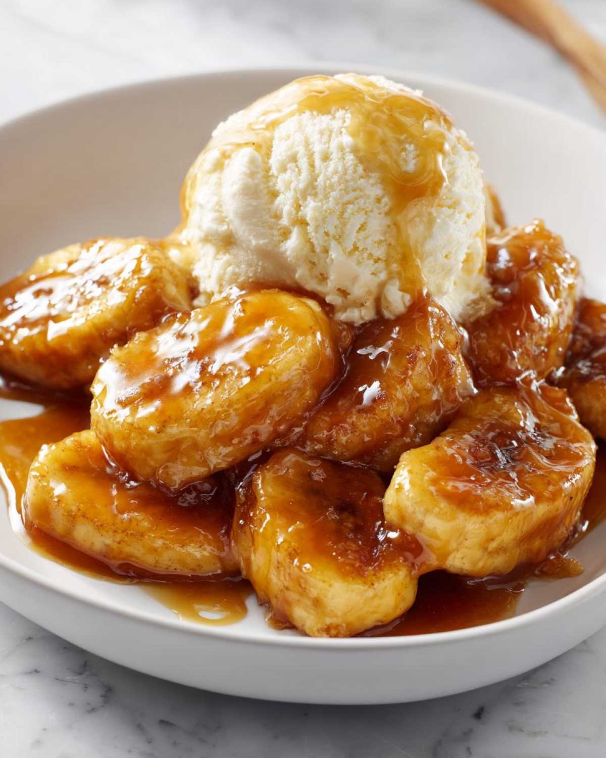 Close-up of caramelized bananas in rich sauce served with a scoop of vanilla ice cream, classic Bananas Foster dessert.