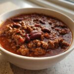A close-up of a white bowl filled with rich, hearty best chili recipe featuring ground meat and kidney beans.