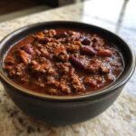 Close-up of a dark bowl filled with rich, meaty chili, featuring ground beef and kidney beans, showcasing the best chili recipe.