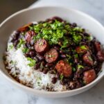 A close-up of a bowl of flavorful black beans and rice topped with sliced sausage and fresh cilantro.