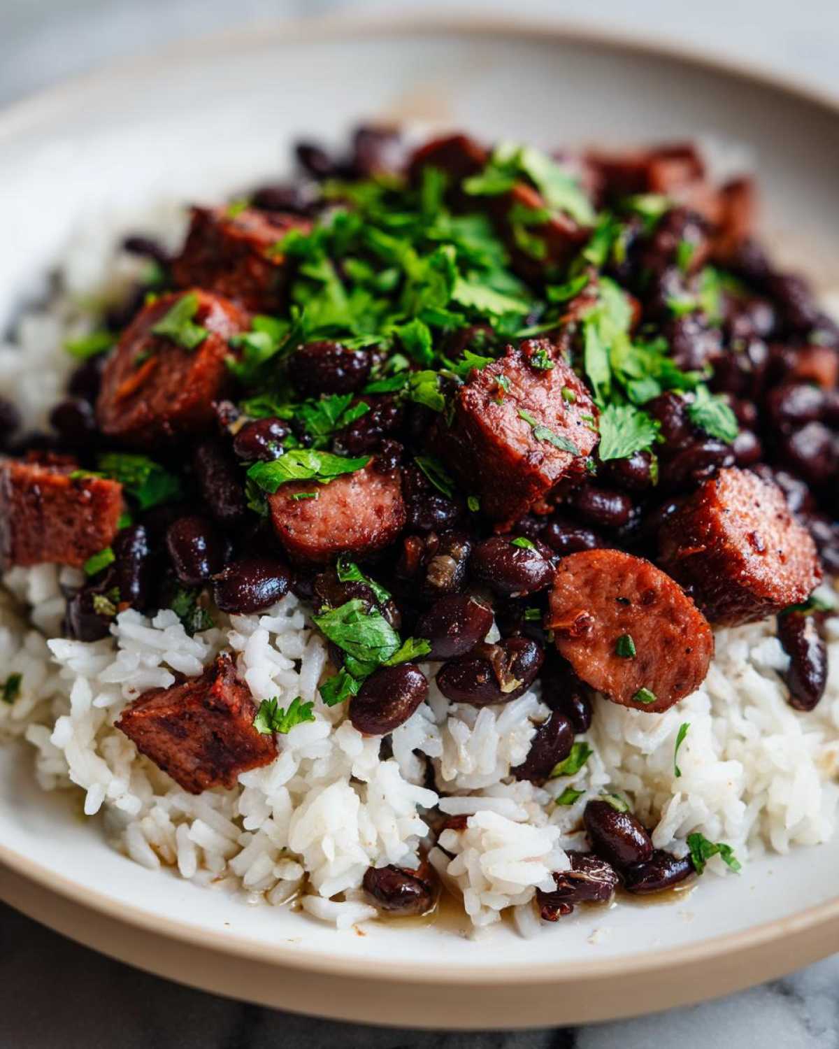 Close-up of a bowl of black beans and rice topped with sliced sausage and fresh cilantro.