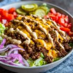 Close-up of a delicious cheeseburger bowl featuring seasoned ground beef, melted cheddar cheese, and special sauce over lettuce.
