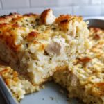 A close-up view of a serving being lifted from a baked cheesy chicken and rice casserole, showing melted cheese and chunks of chicken.