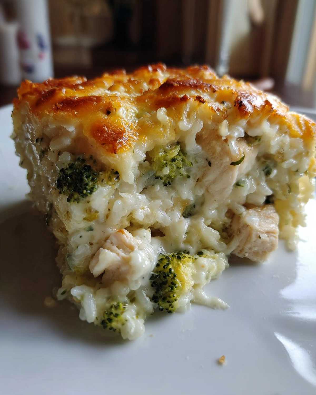 A close-up view of a serving of creamy chicken broccoli rice casserole topped with melted, golden-brown cheese.