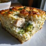A close-up, appetizing slice of chicken broccoli rice casserole with a golden-brown crust.