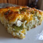 A close-up of a square slice of creamy chicken broccoli rice casserole topped with melted cheddar cheese.