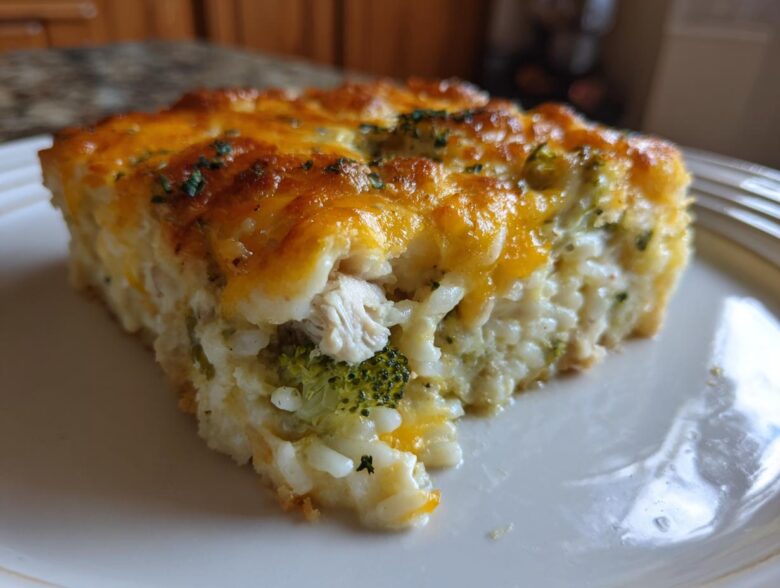A close-up of a square slice of creamy chicken broccoli rice casserole topped with melted cheddar cheese.