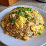 A close-up of a serving of delicious chicken fried rice mixed with scrambled egg pieces and topped with fresh green onions.