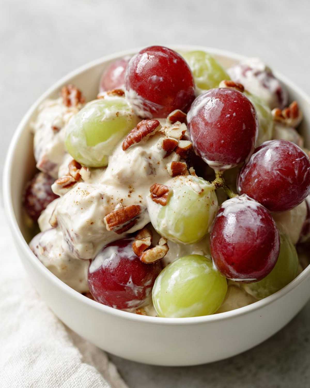 Close-up of creamy chicken salad chick grape salad featuring red and green grapes coated in dressing and topped with chopped pecans.