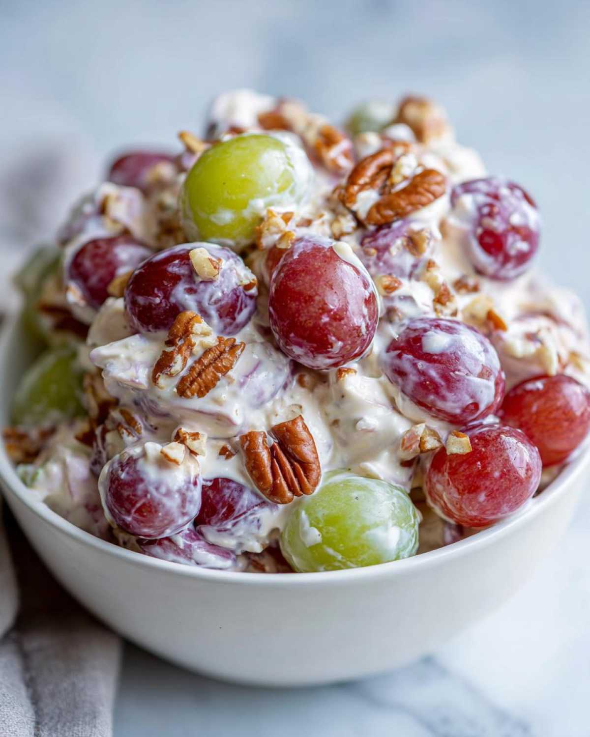 Close-up of creamy chicken salad chick grape salad featuring red and green grapes mixed with a creamy dressing and topped with pecans.