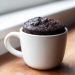 A rich, dark chocolate mug cake baked perfectly inside a simple white mug.