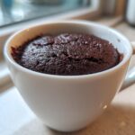 Close-up of a rich, dark chocolate mug cake baked inside a white ceramic mug.