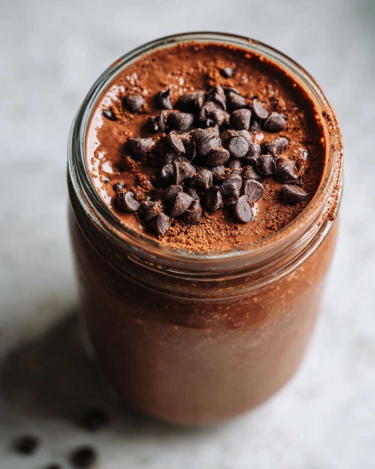 Close-up of rich chocolate overnight oats in a jar, topped generously with chocolate chips and cocoa powder.