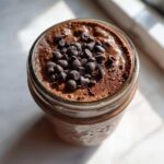 Overhead view of rich chocolate overnight oats in a jar, topped generously with mini chocolate chips.