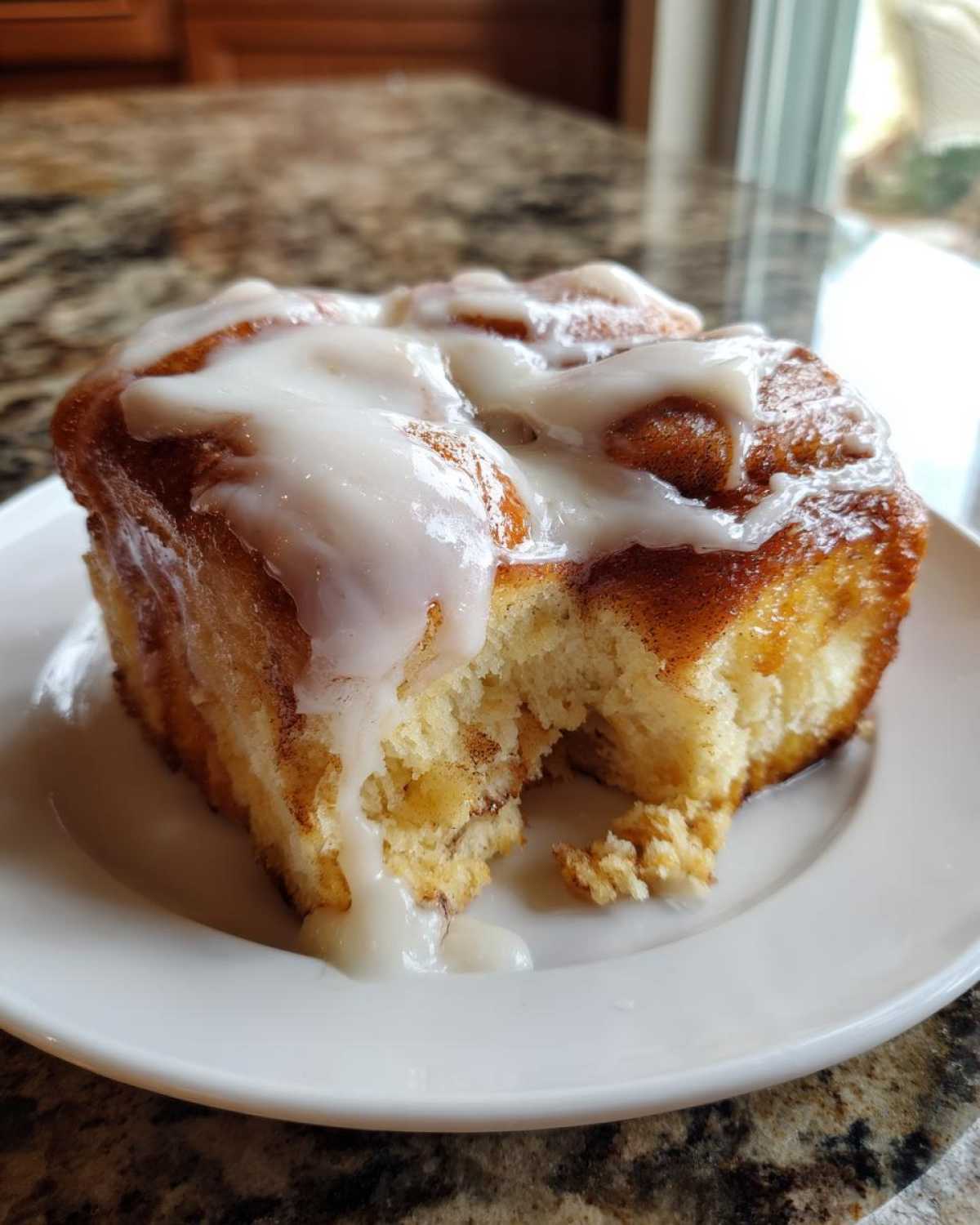Close-up of a square serving of soft Cinnamon roll casserole topped with dripping white icing on a white plate.