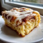 Close-up of a single, fluffy square slice of cinnamon roll casserole topped with thick white icing.