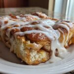 A generous slice of warm Cinnamon roll casserole topped with thick, dripping vanilla icing on a white plate.