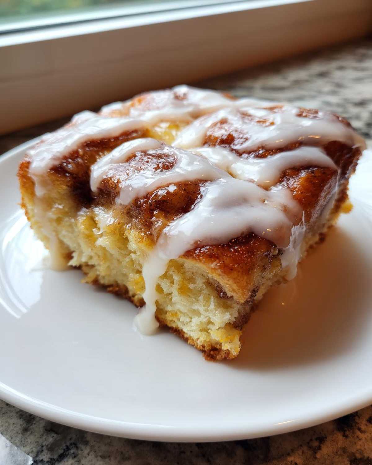 A close-up slice of warm Cinnamon roll casserole topped with thick white vanilla icing.