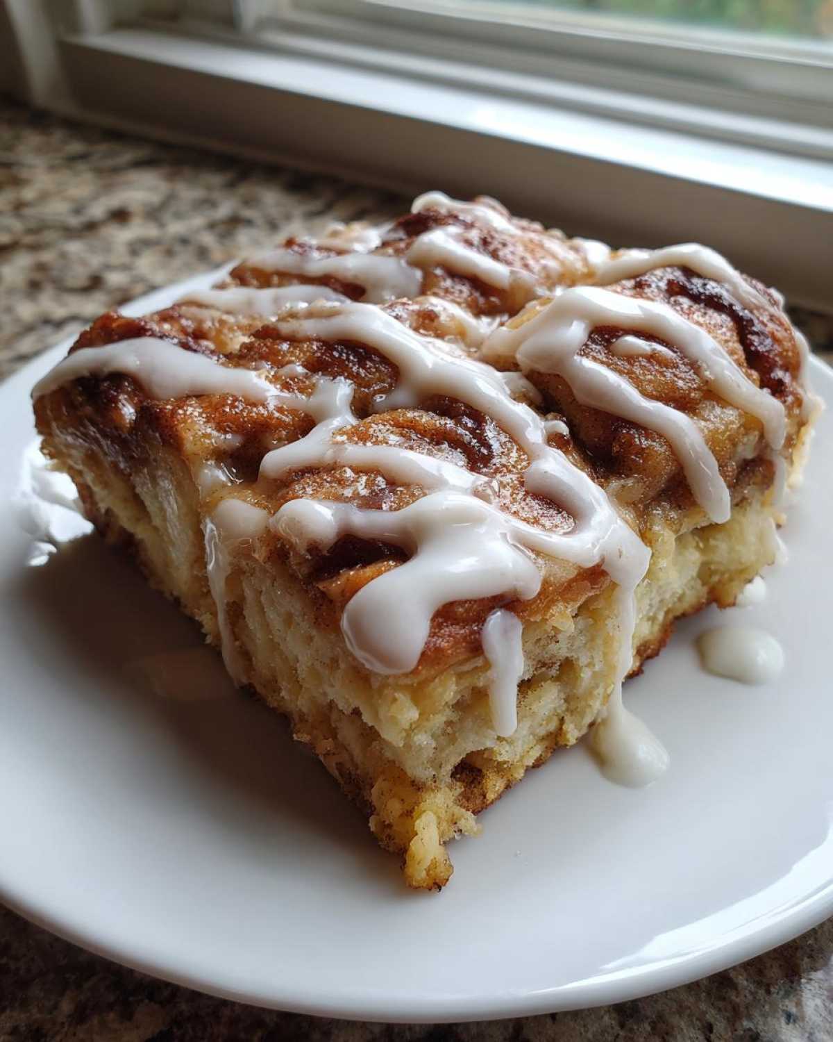 A close-up of a square slice of gooey Cinnamon roll casserole topped with thick white icing.