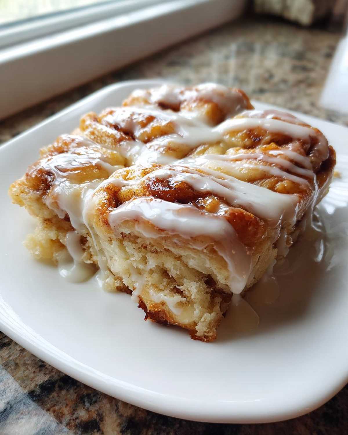 A close-up of a gooey slice of cinnamon roll casserole topped with thick white icing.