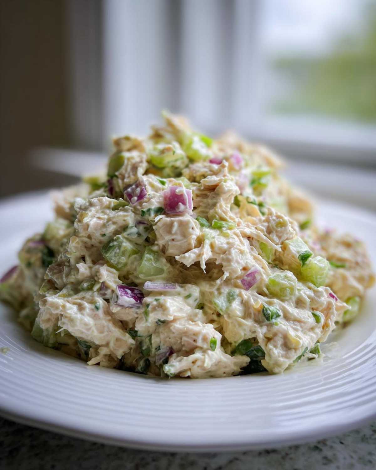 A heaping scoop of creamy cottage cheese chicken salad featuring chunks of chicken, celery, and red onion on a white plate.